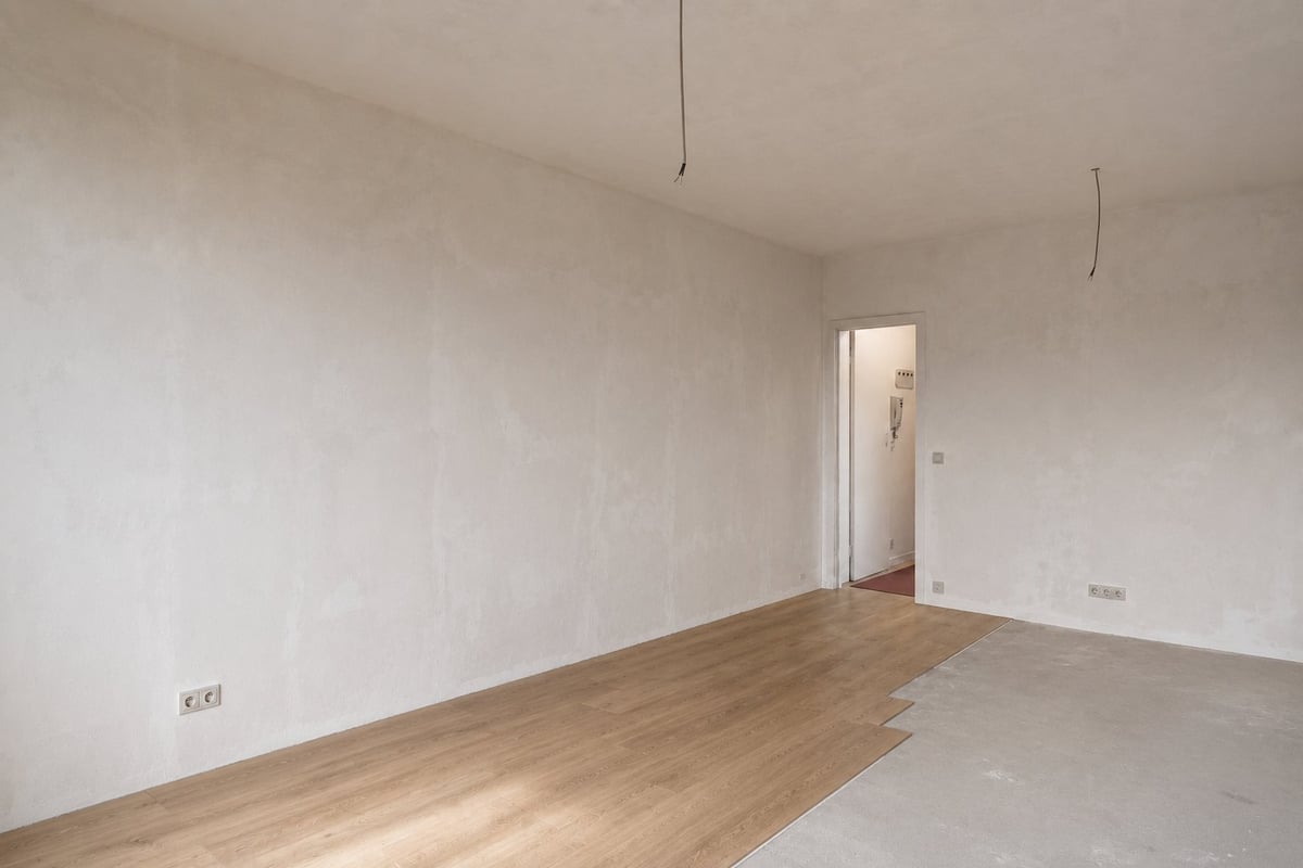 Empty room with white walls, partially installed laminate flooring, open doorway, and wall outlets visible